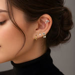 A woman's ear with a curated stack featuring Lark & Berry's gold Evil Eye earrings with diamond drops and a helix stud.