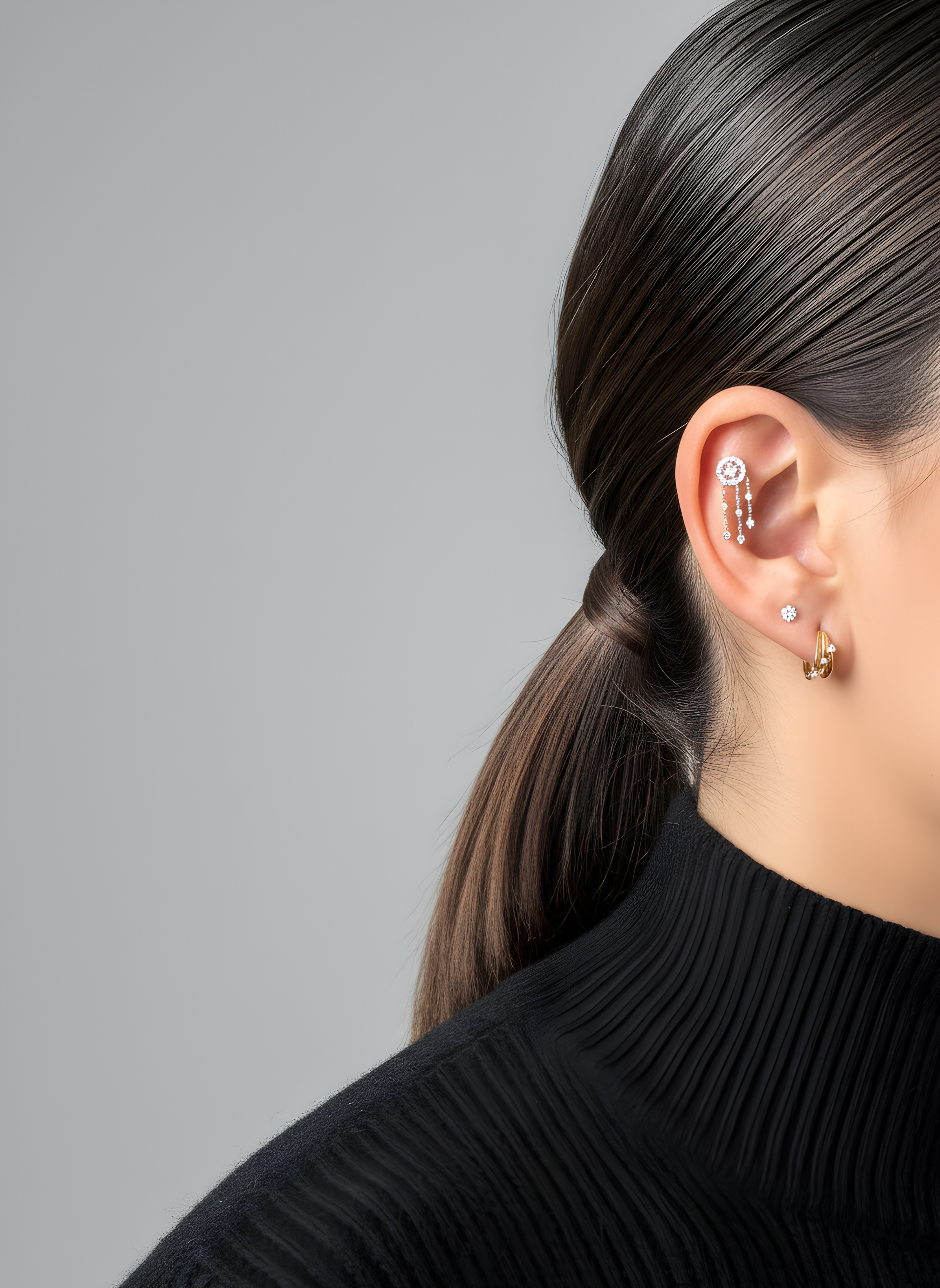 Woman's ear with Lark & Berry's Dreamcatcher Diamond Drop helix earring, a diamond stud, and a small gold hoop.