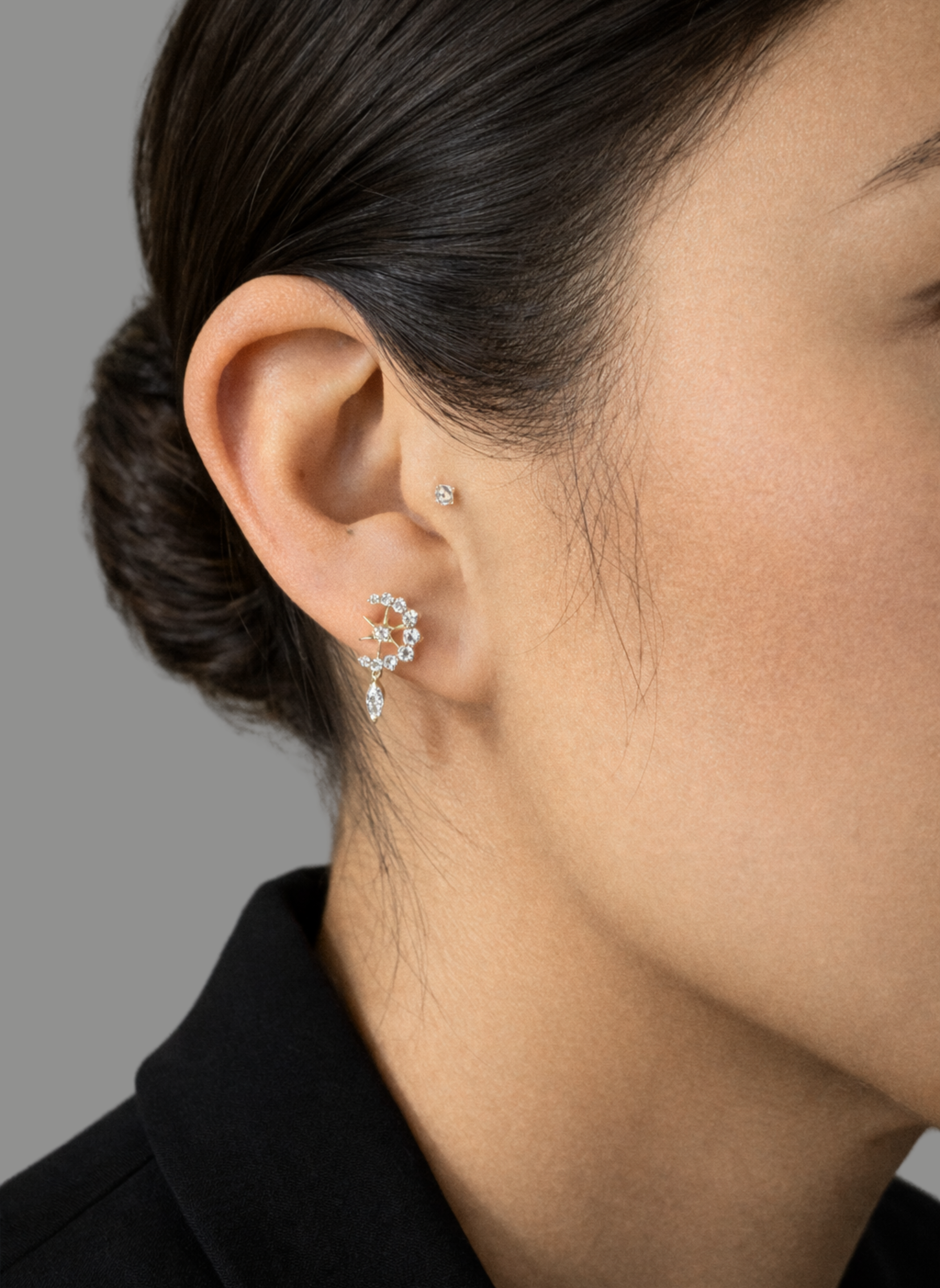 Model's ear wearing the gold Entwined Diamond Moon and Star Stud earring with a dangling diamond against a grey background.