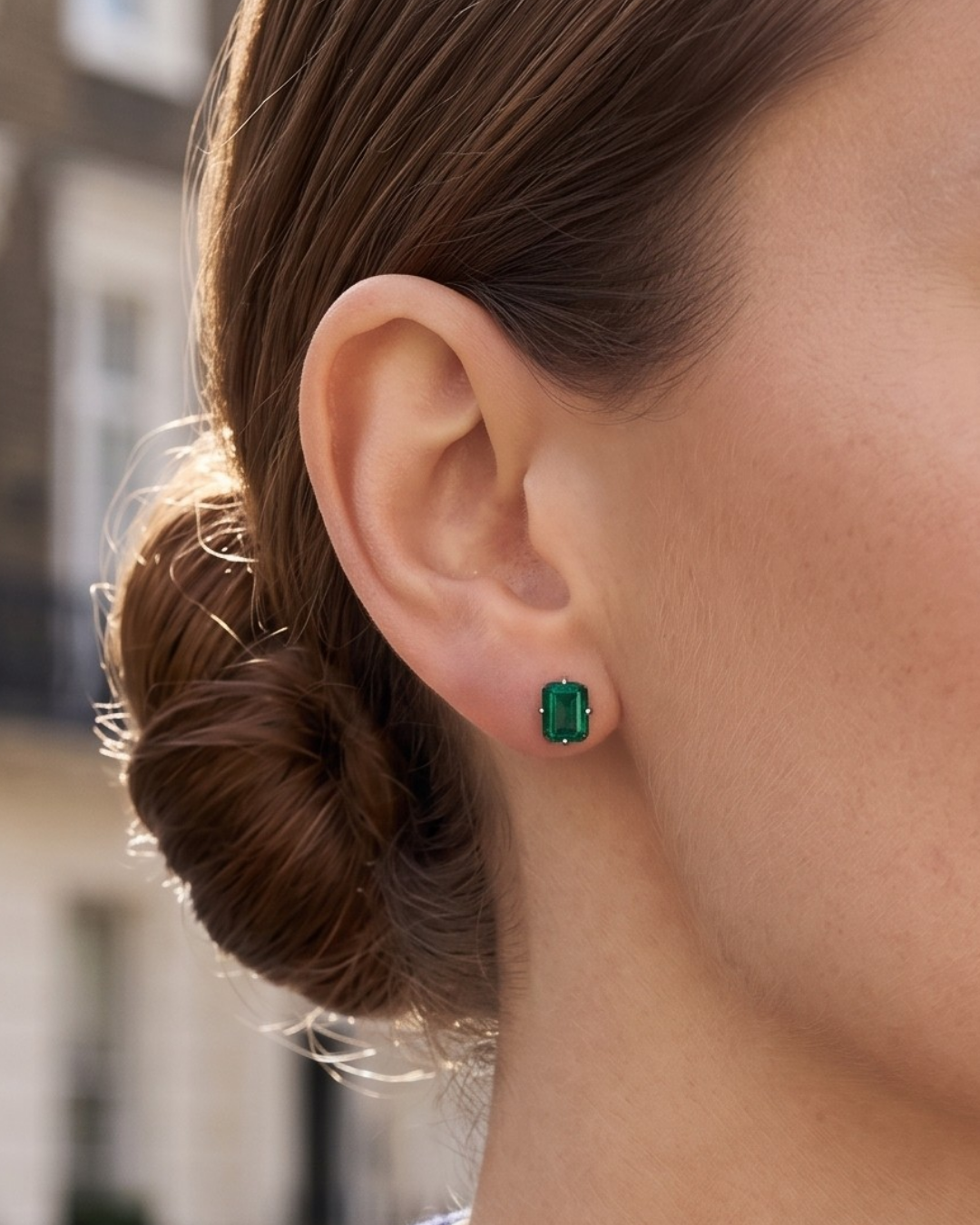 Close-up of a woman wearing a rectangular London Bridge Emerald Stud earring, with her brown hair pulled back in a bun.