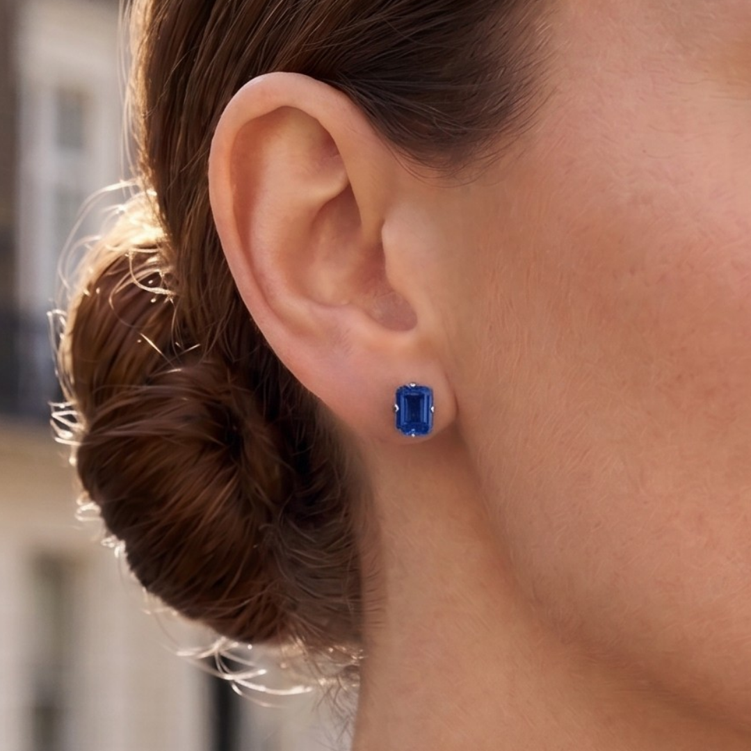 A woman wears a Lark & Berry London Bridge Blue Sapphire Stud earring with a bright, emerald-cut stone.