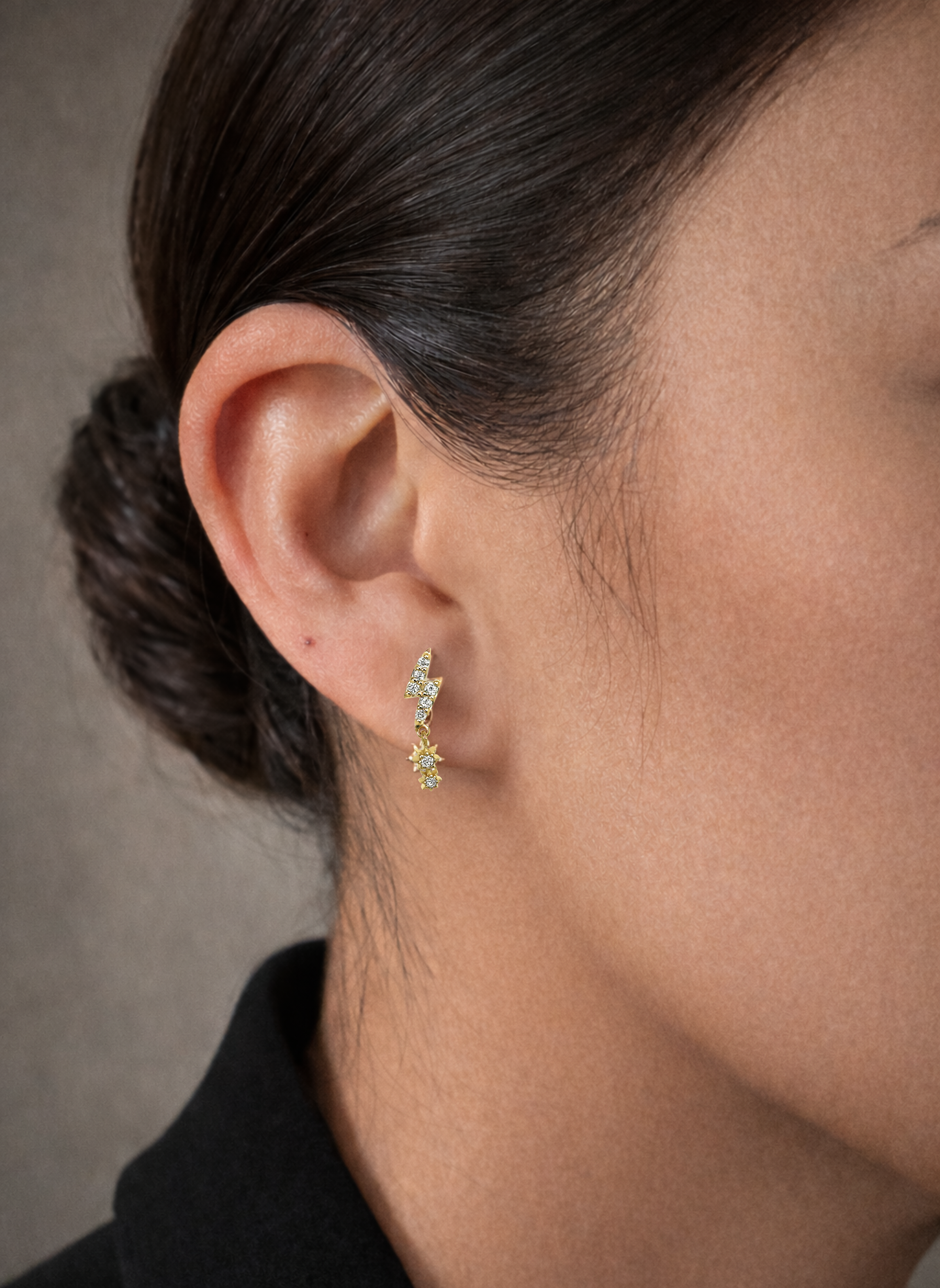 A model's ear with the Lark & Berry Lightening Bolt diamond drop earring in gold, featuring a starburst charm.