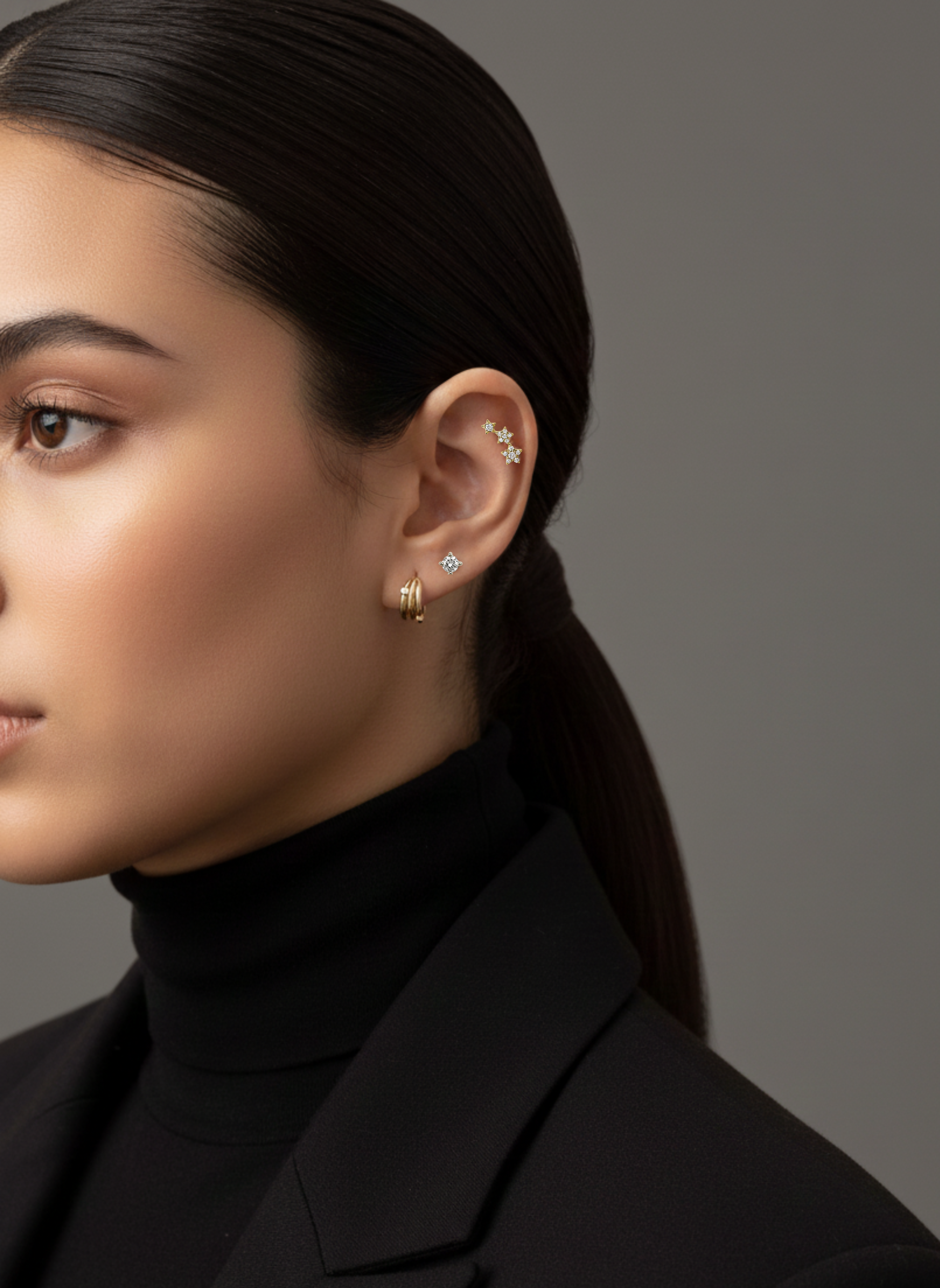 A model's ear styled with Lark & Berry's 3-Star Diamond Stud, a single diamond stud, and a gold hoop earring.